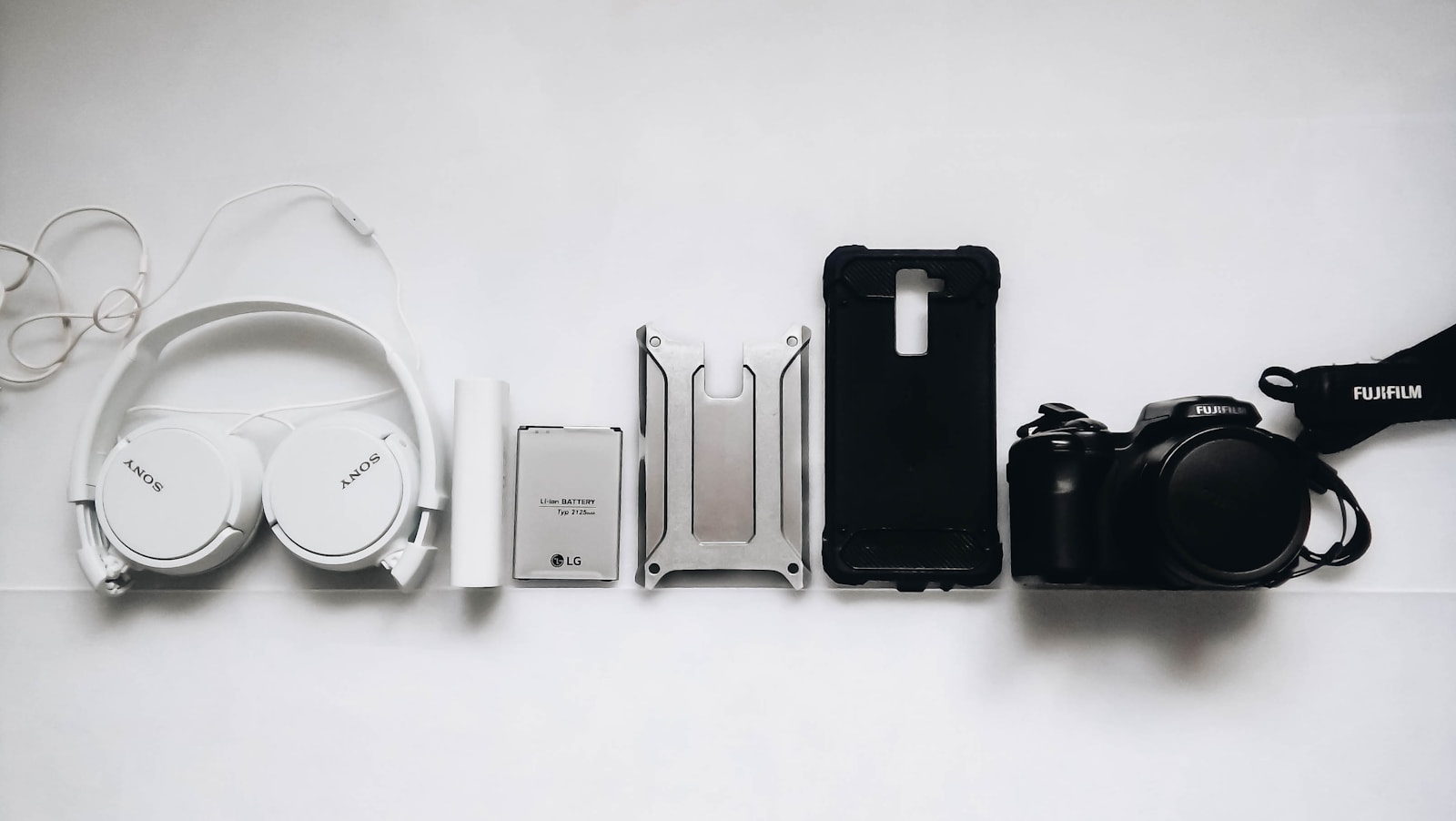 White Sony headphones, phone case, battery, and camera laid out on a table