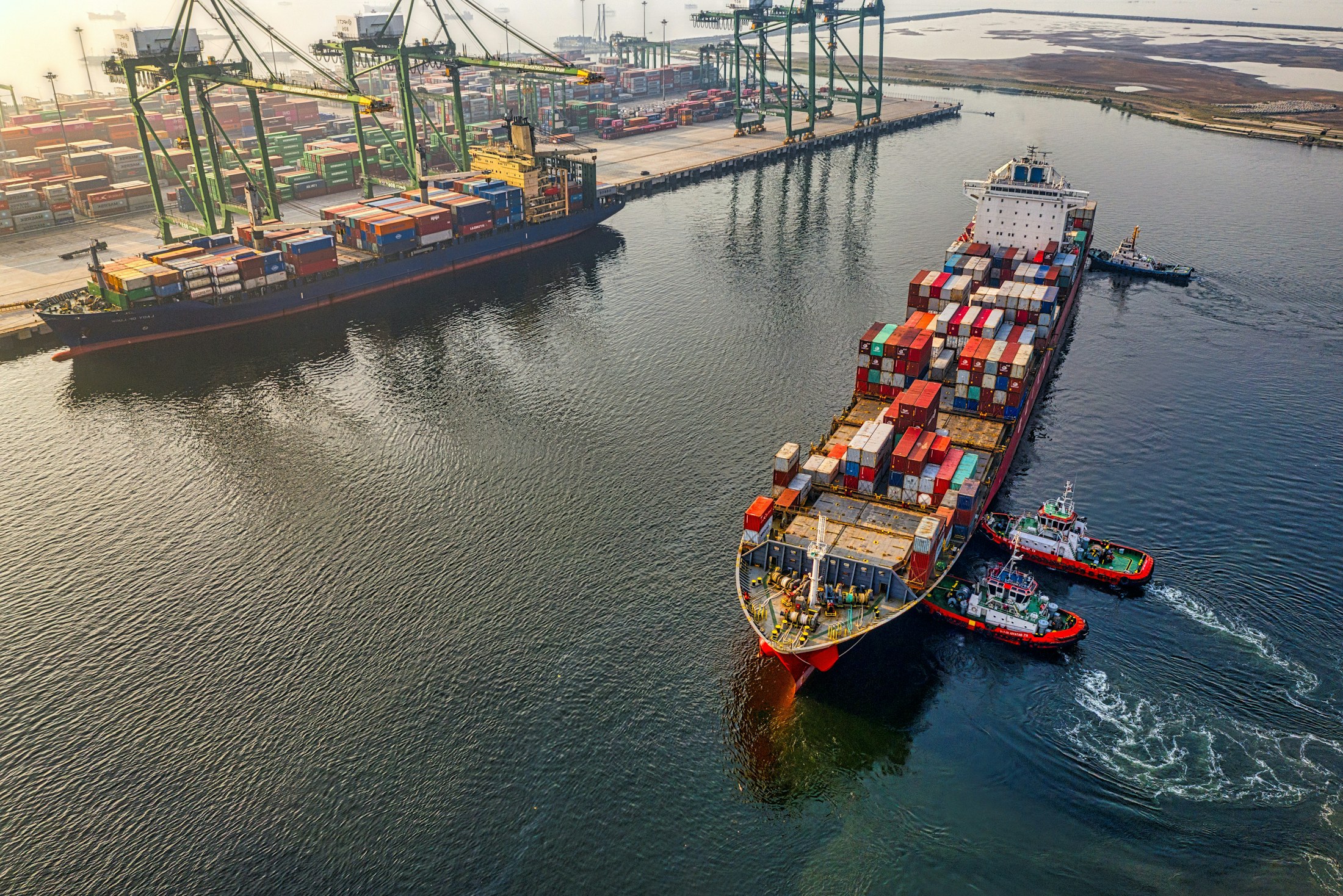 Container ship moving through a port with cranes and stacked containers