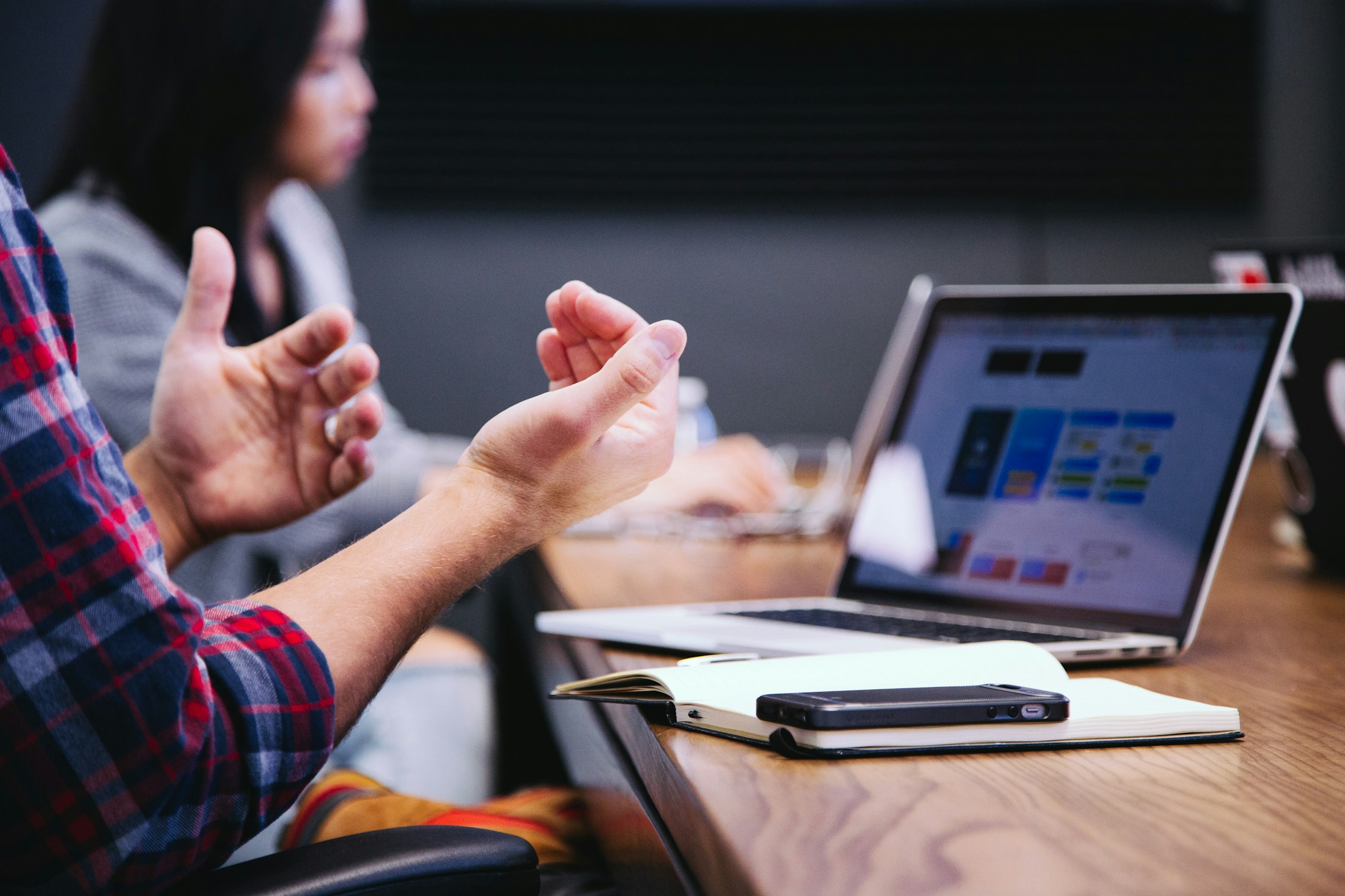 Person gesturing during a meeting with a laptop on the table